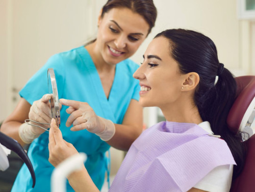 Une femme sur une chaise de dentiste qui regarde dans un miroir son sourire.